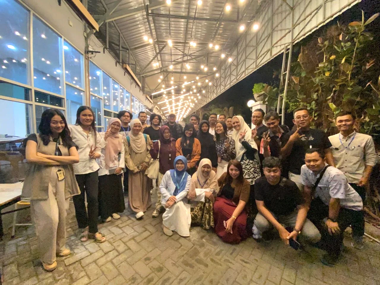 Anggota komunitas berfoto bersama di ruang terbuka dengan lampu hangat.