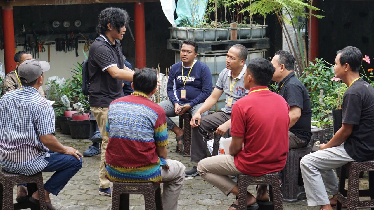 Peserta duduk melingkar dan menyimak seseorang yang sedang berbicara.