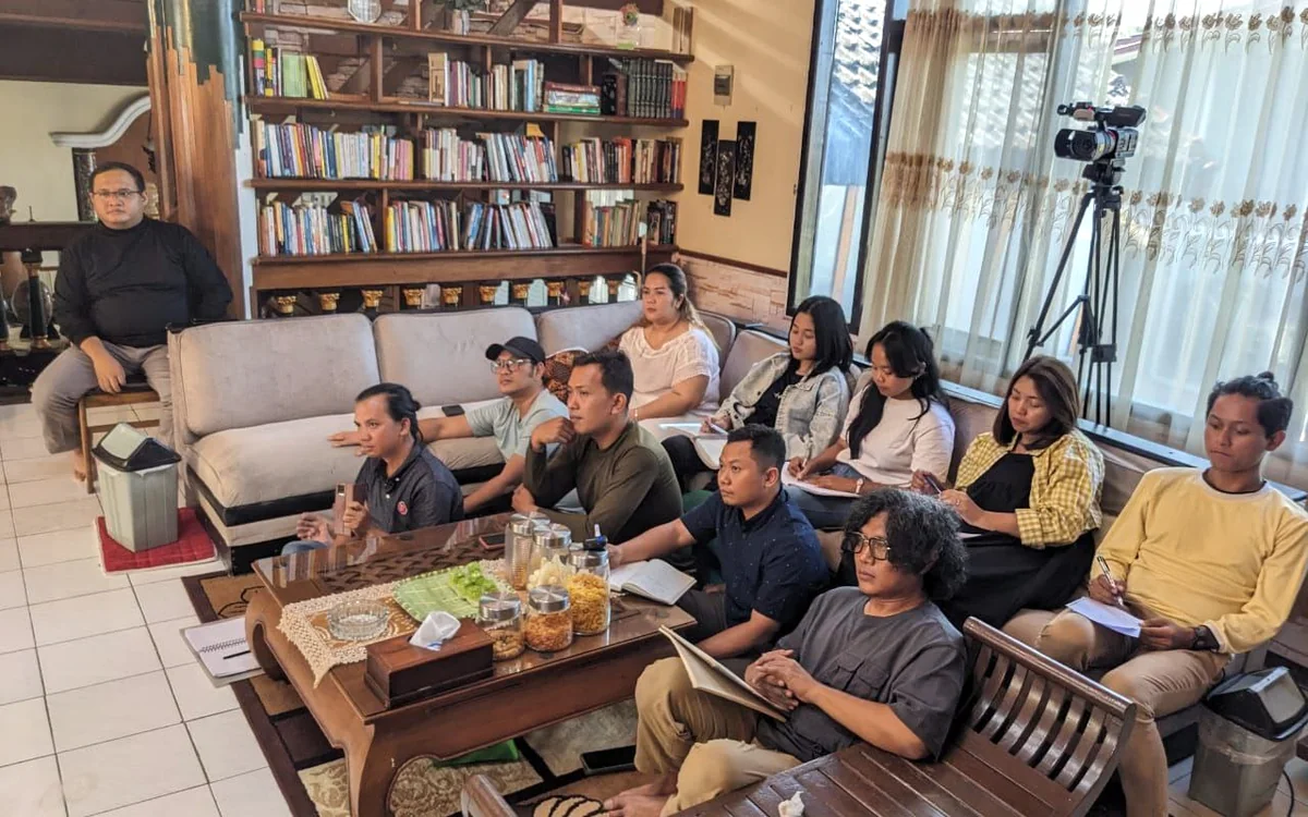 Peserta duduk dengan catatan di ruangan yang memiliki rak buku.