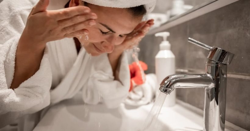 young-beautiful-woman-bathroom-with-towel-her-head-washes-her-face-with-tap-water_169016-10604